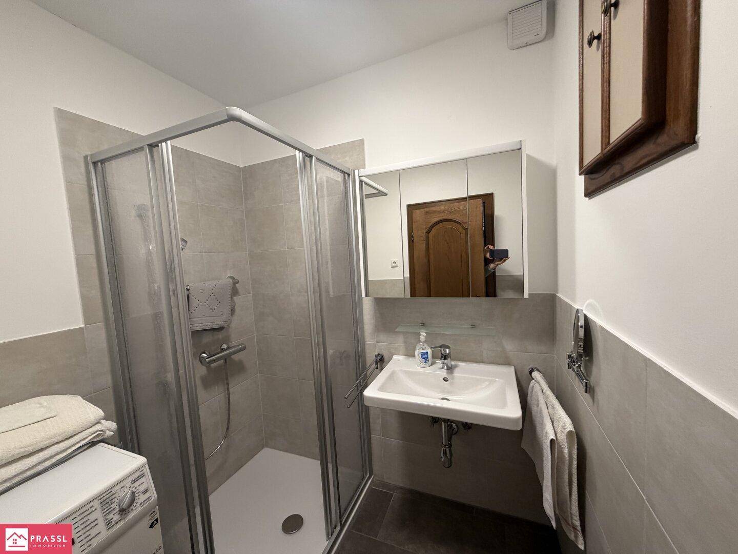 Modernisiertes Badezimmer mit Duschkabine, Waschbecken und Waschmaschine.