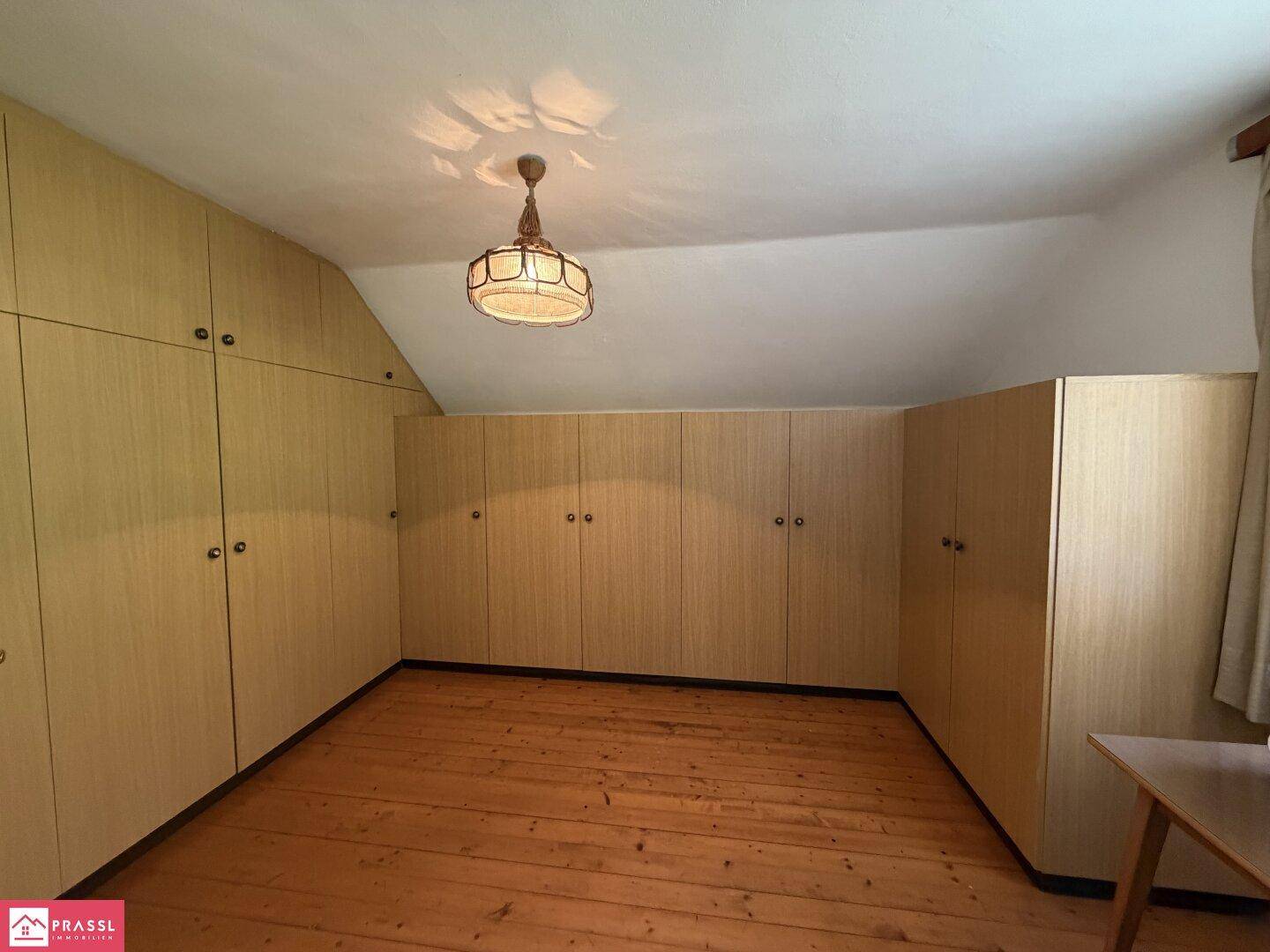 Zimmer im Dachgeschoss mit vielen Einbauschränken und Holzboden.