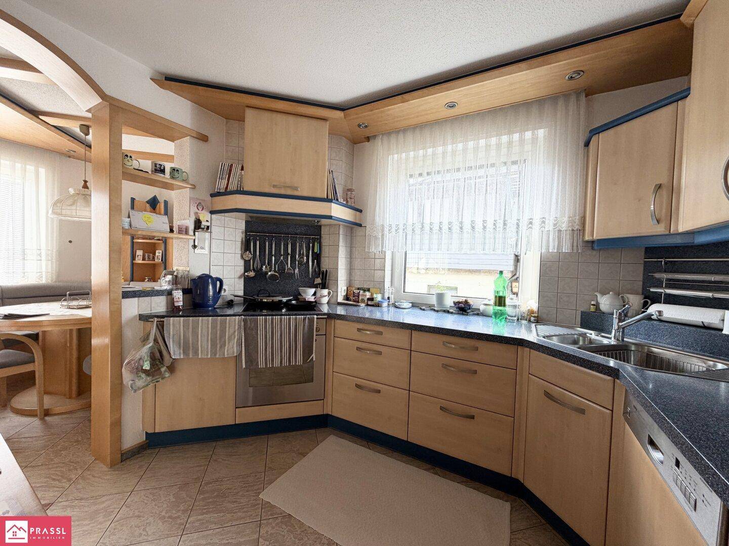 Funktionale Küche mit Holzfronten, dunkler Arbeitsplatte und Fenster mit Blick ins Grüne.
