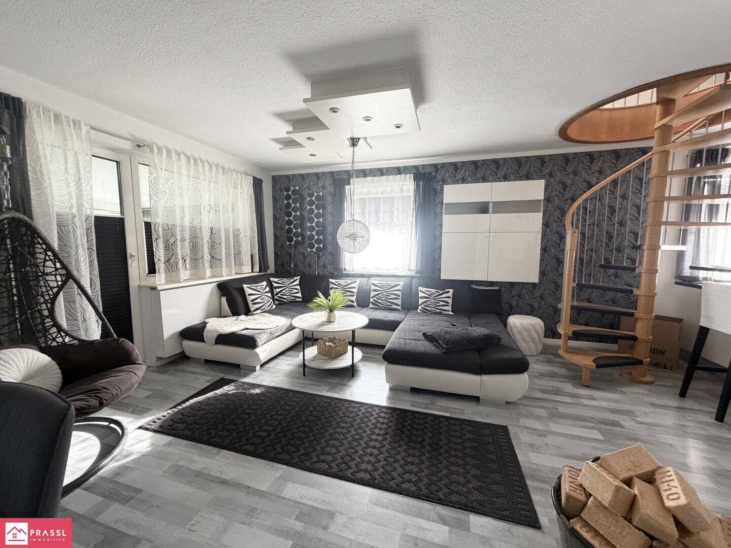 Heller Wohnbereich mit modernem Sofa, Hängesessel und einer eleganten Wendeltreppe.