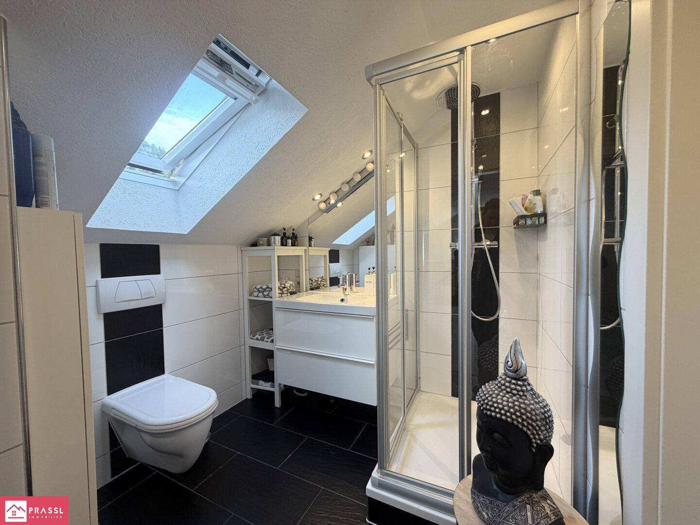 Modernes Badezimmer im Dachgeschoss mit Dusche, WC, Waschtisch und Dachfenster.