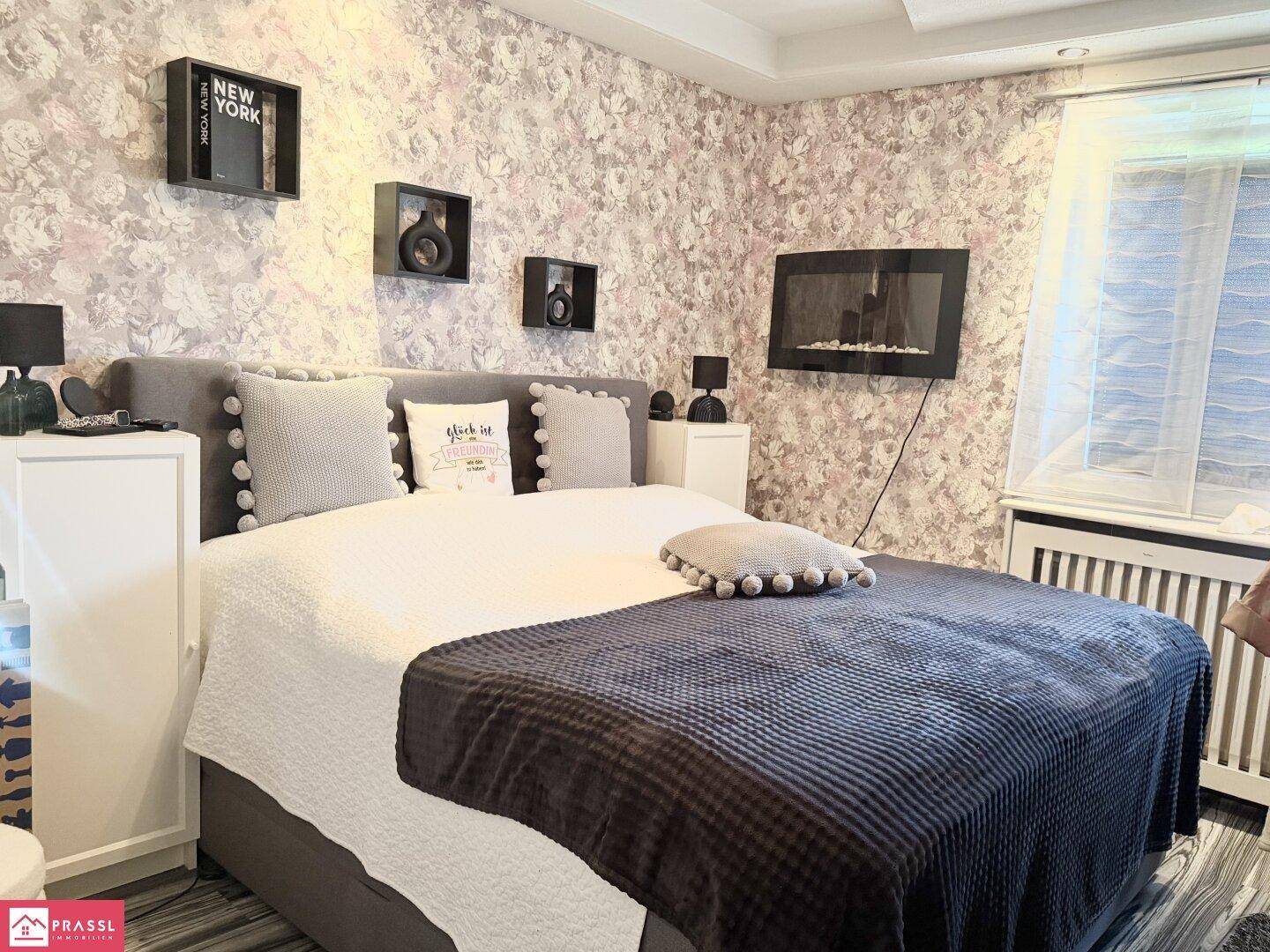 Gemütliches Schlafzimmer mit floraler Tapete, großem Bett und dekorativen Elementen.