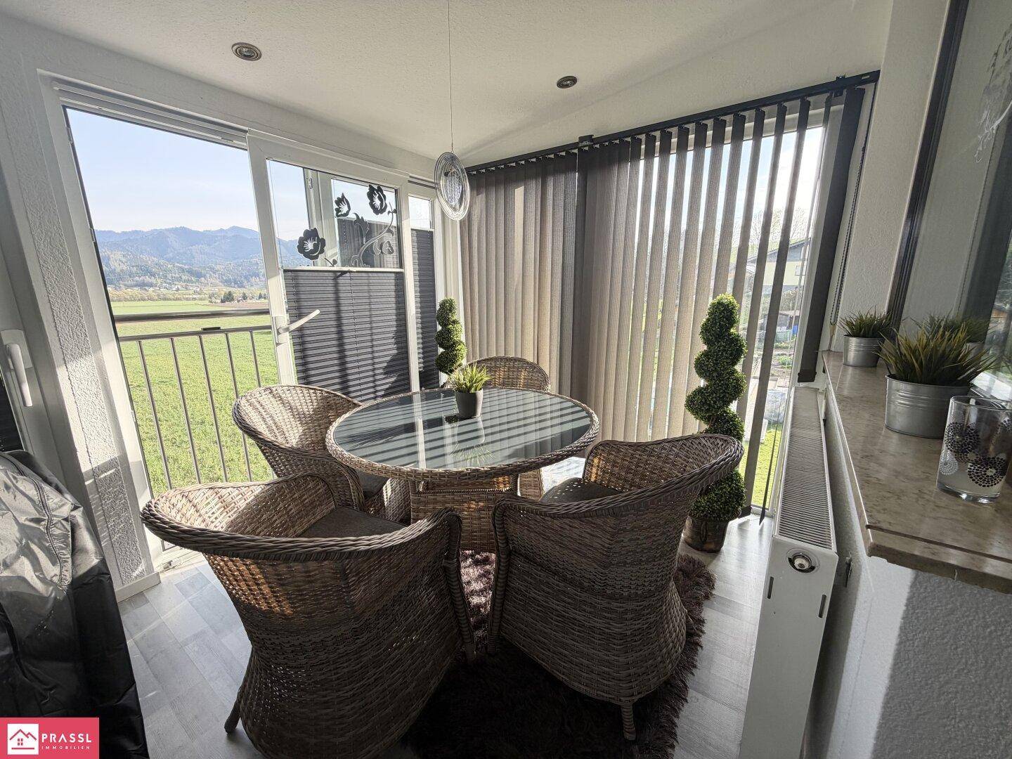 Heller Wintergarten mit Rattanmöbeln und weitem Blick auf die grüne Landschaft.