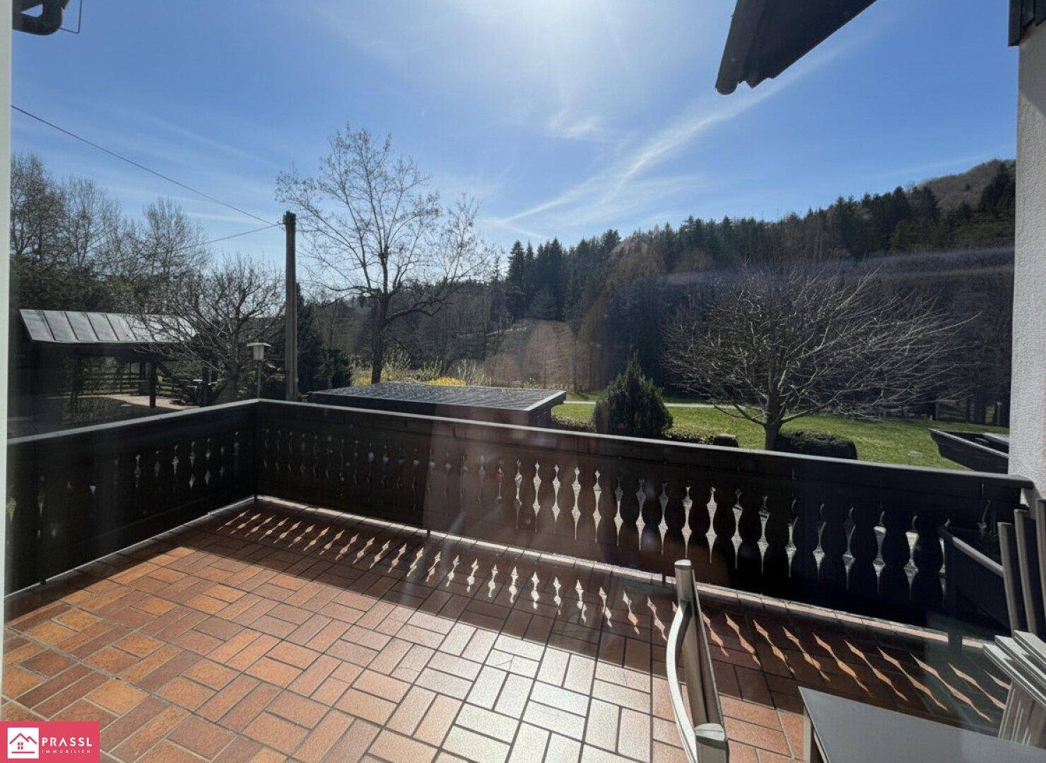 Sonniger Balkon mit Terrakottafliesen und weitem Blick ins Grüne und auf die umliegende Landschaft.