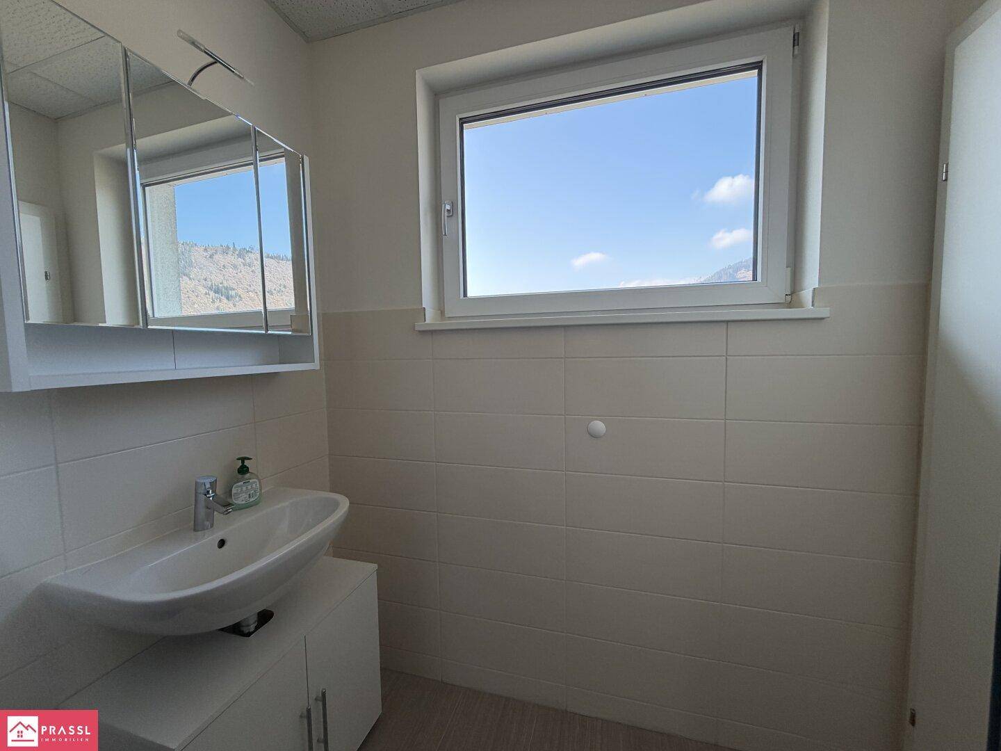 Helles Badezimmer mit Fenster, Waschbeckenunterschrank und Spiegelschrank, bietet einen Bergblick.