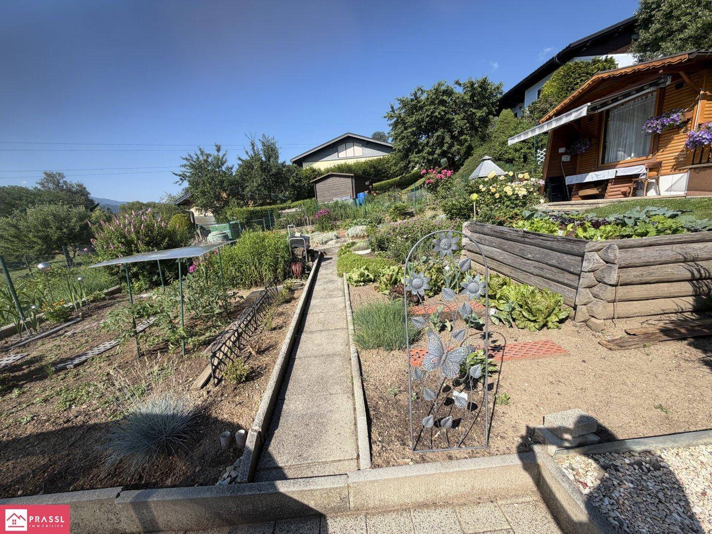 Terrassierter Nutzgarten mit Hochbeeten, Wegen und einem kleinen Gartenhaus im Grünen.