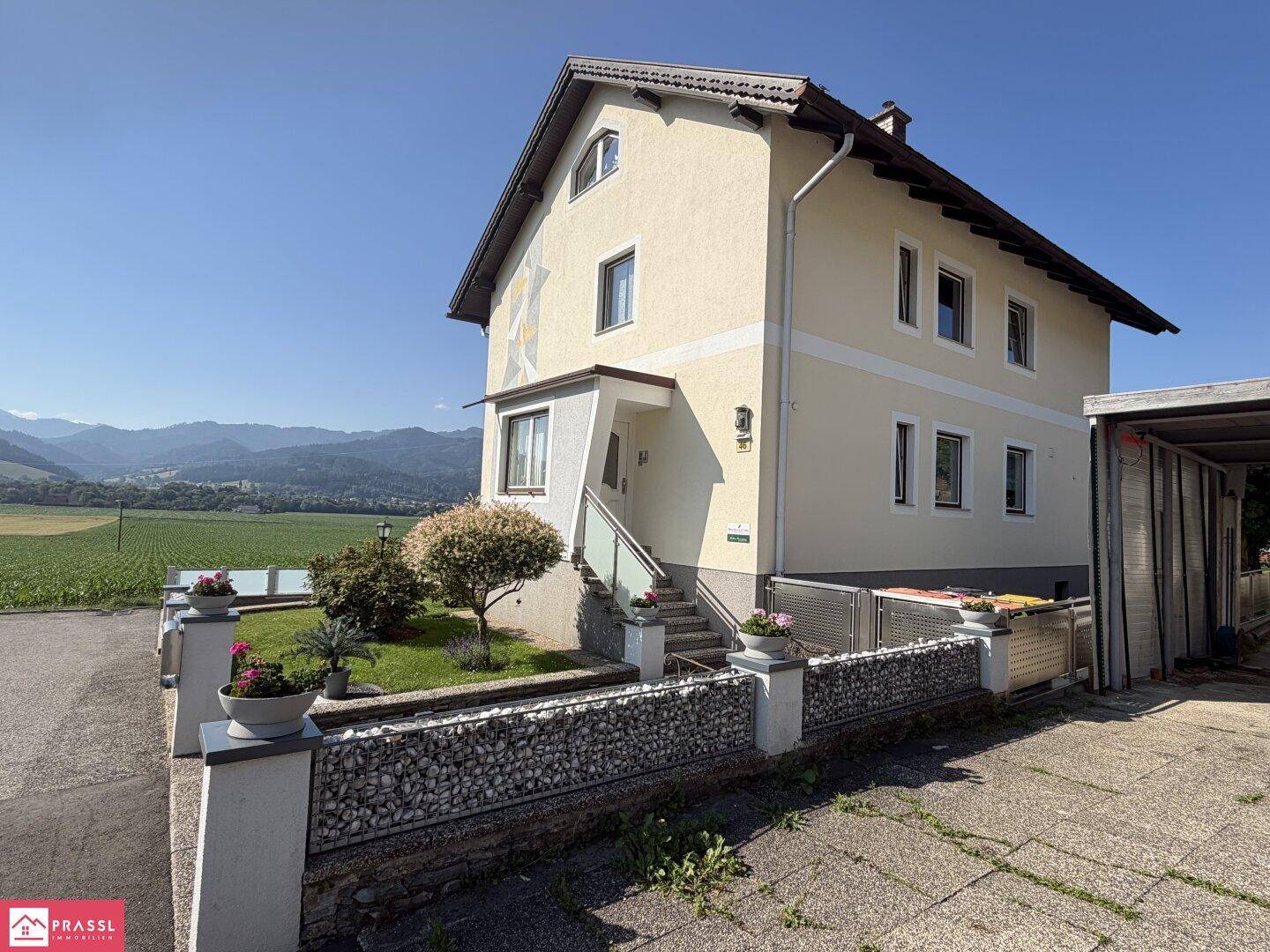 Vorderansicht des Hauses mit Eingangsbereich, kleinem Vorgarten und ländlichem Ausblick.