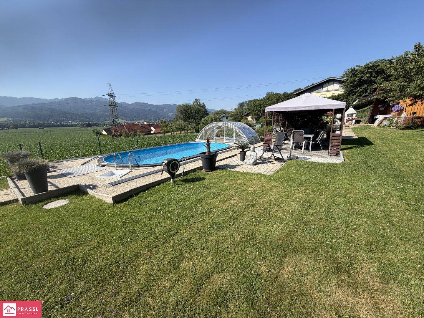Großer Gartenbereich mit Pool, Pavillon und Sitzgelegenheiten, umgeben von grüner Landschaft.