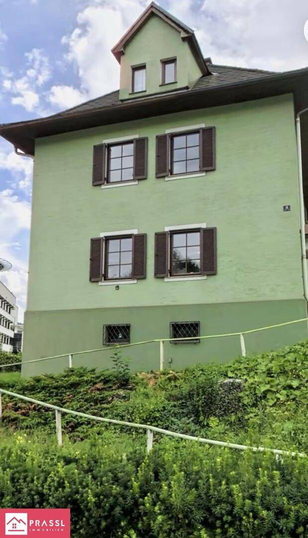 Nahaufnahme der grünen Fassade eines Hauses mit braunen Fensterläden und Dachgaube.