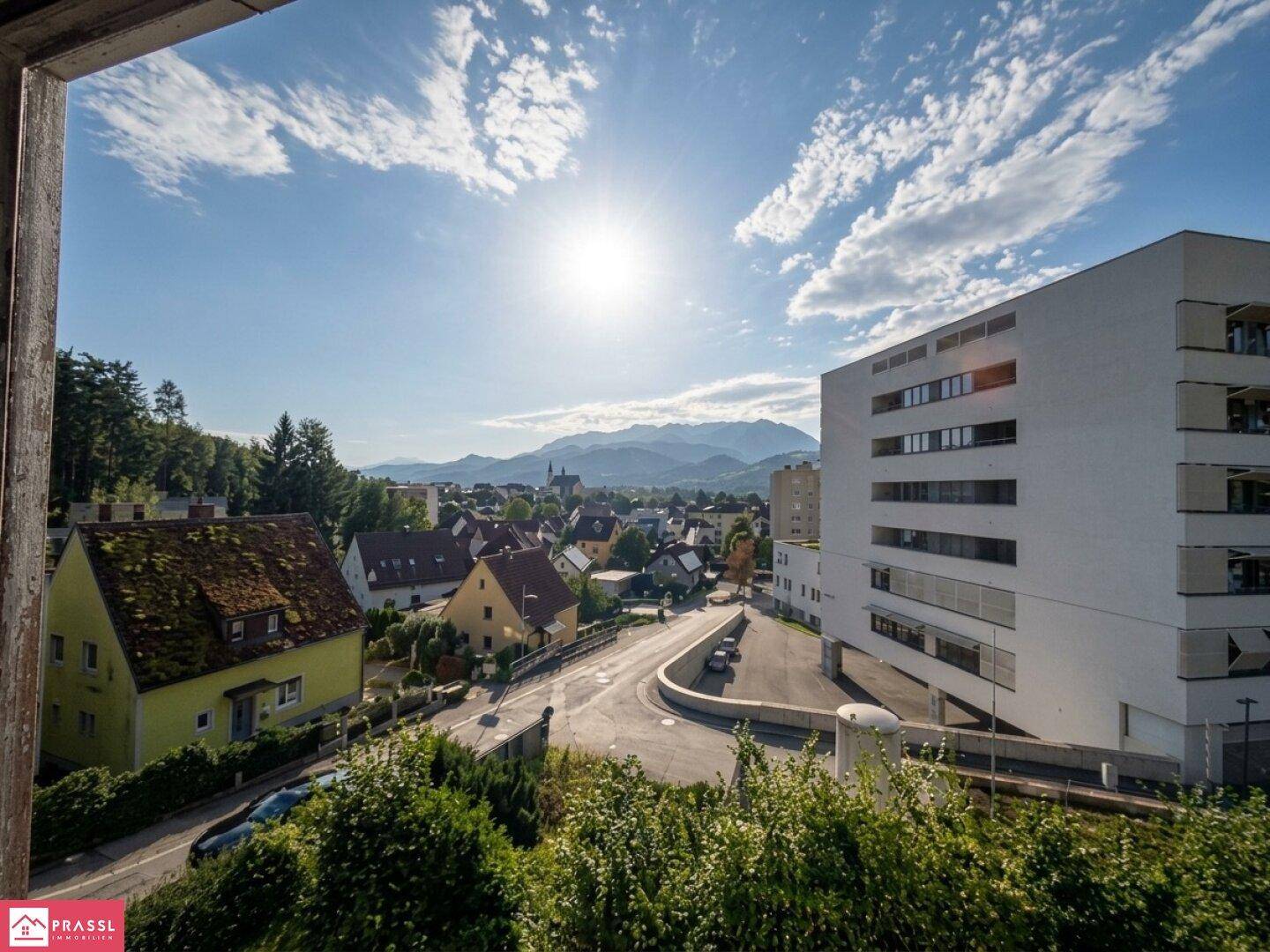 Weitblick über eine Stadt mit Bergen im Hintergrund, gesehen durch ein Fenster.