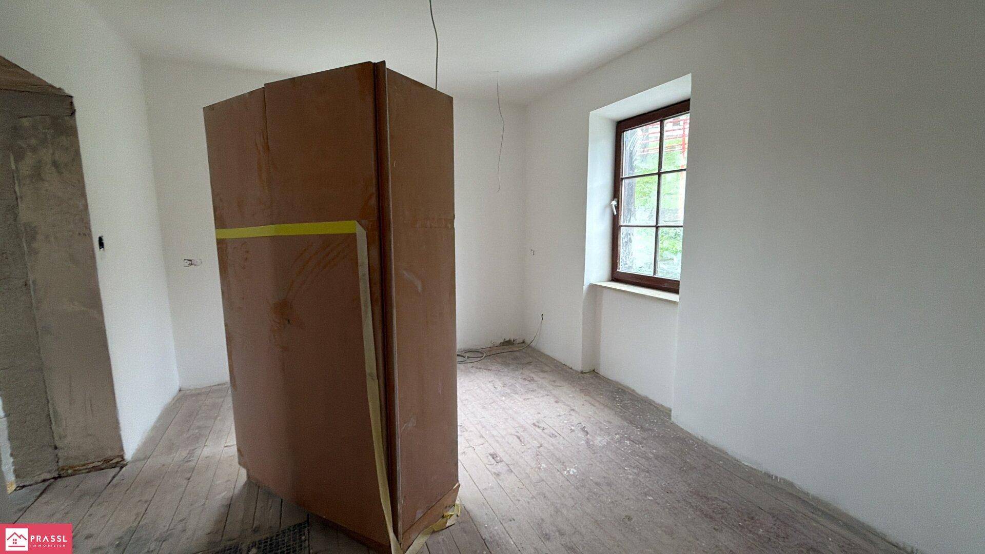Leerer Raum in Renovierung mit einem großen Karton in der Mitte und Holzboden.