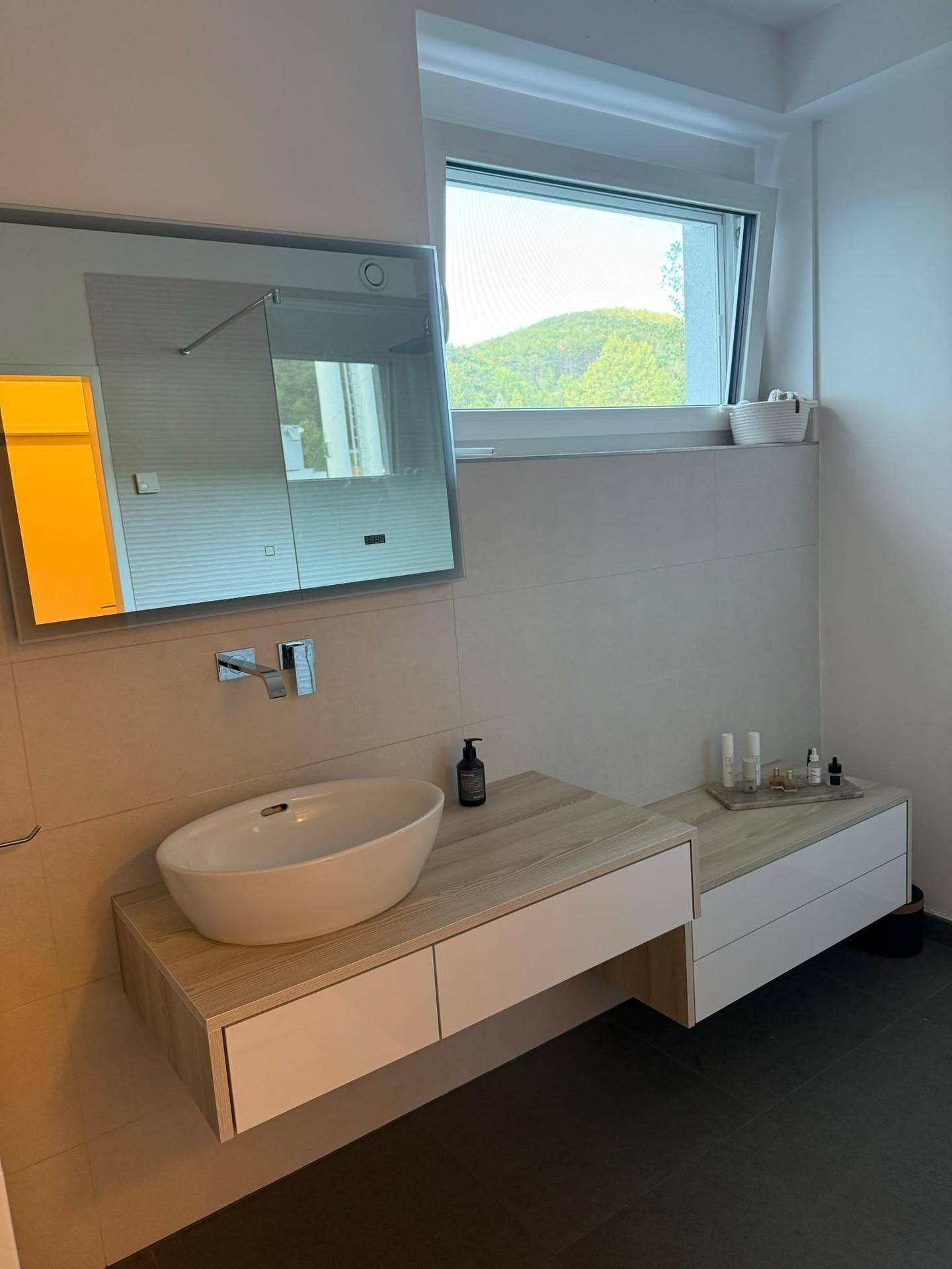 Helles Badezimmer mit modernem Waschtisch, großem Spiegel und Fenster.