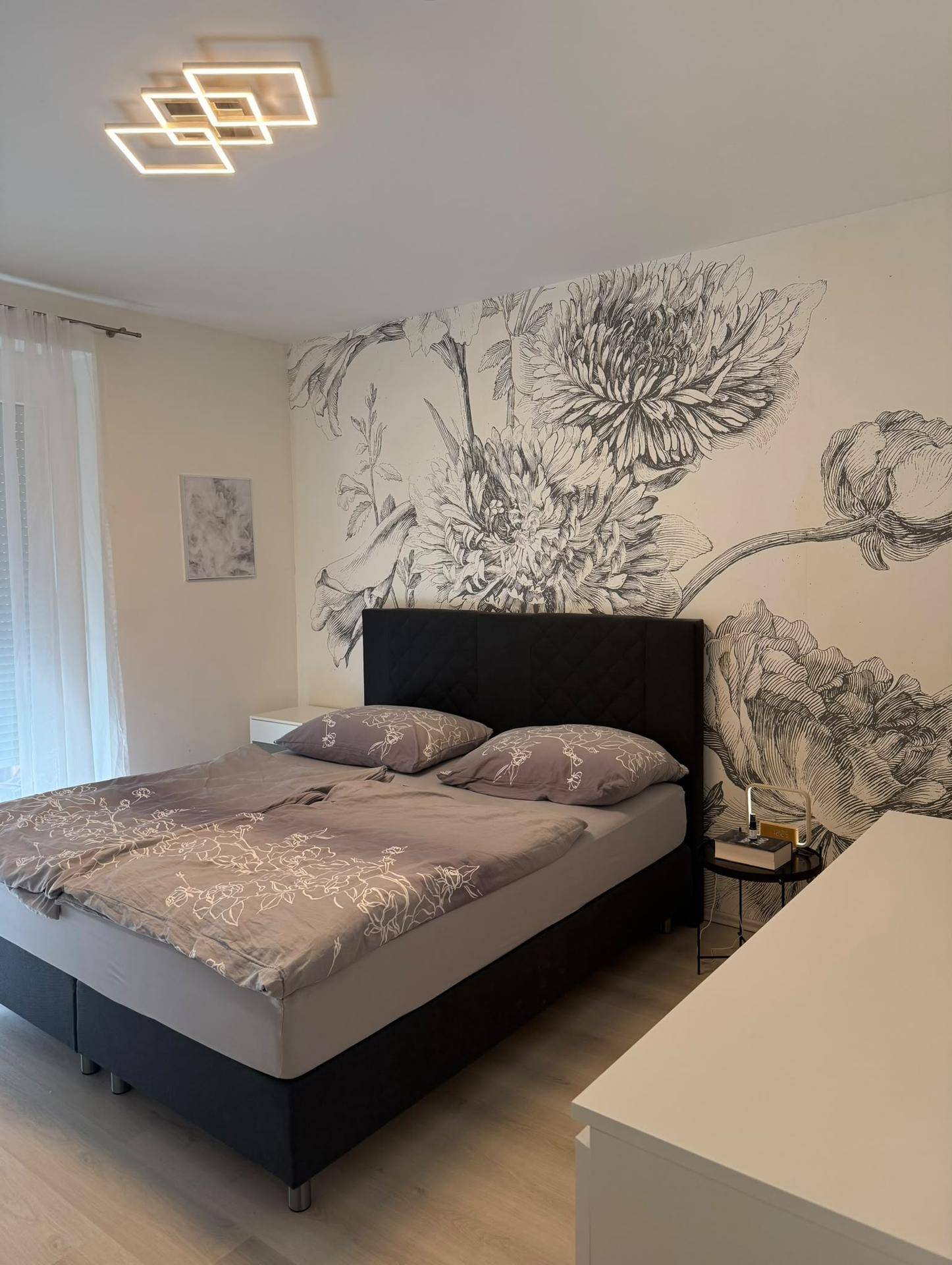 Schlafzimmer mit Doppelbett, floraler Wanddekoration und hellem Laminatboden.