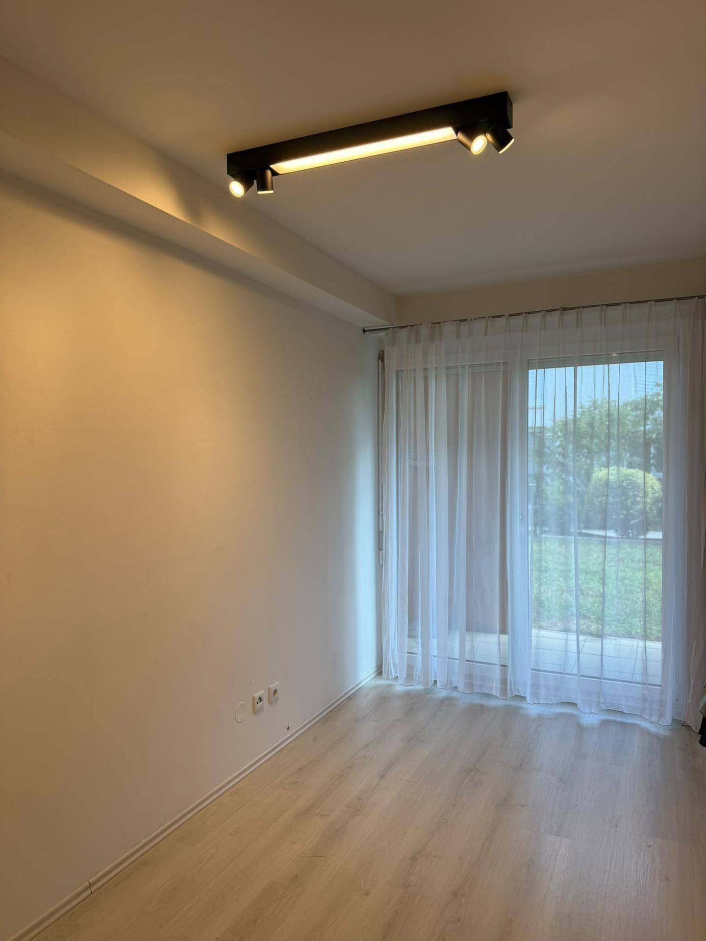 Helles Zimmer mit Laminatboden und Zugang zu einem Außenbereich.