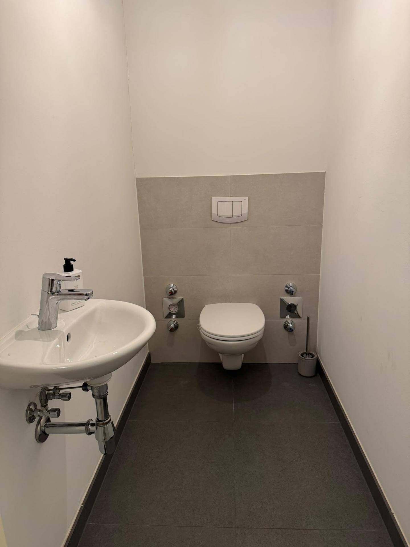 Separates Gäste-WC mit Wand-WC, kleinem Waschbecken und dunklem Fliesenboden.