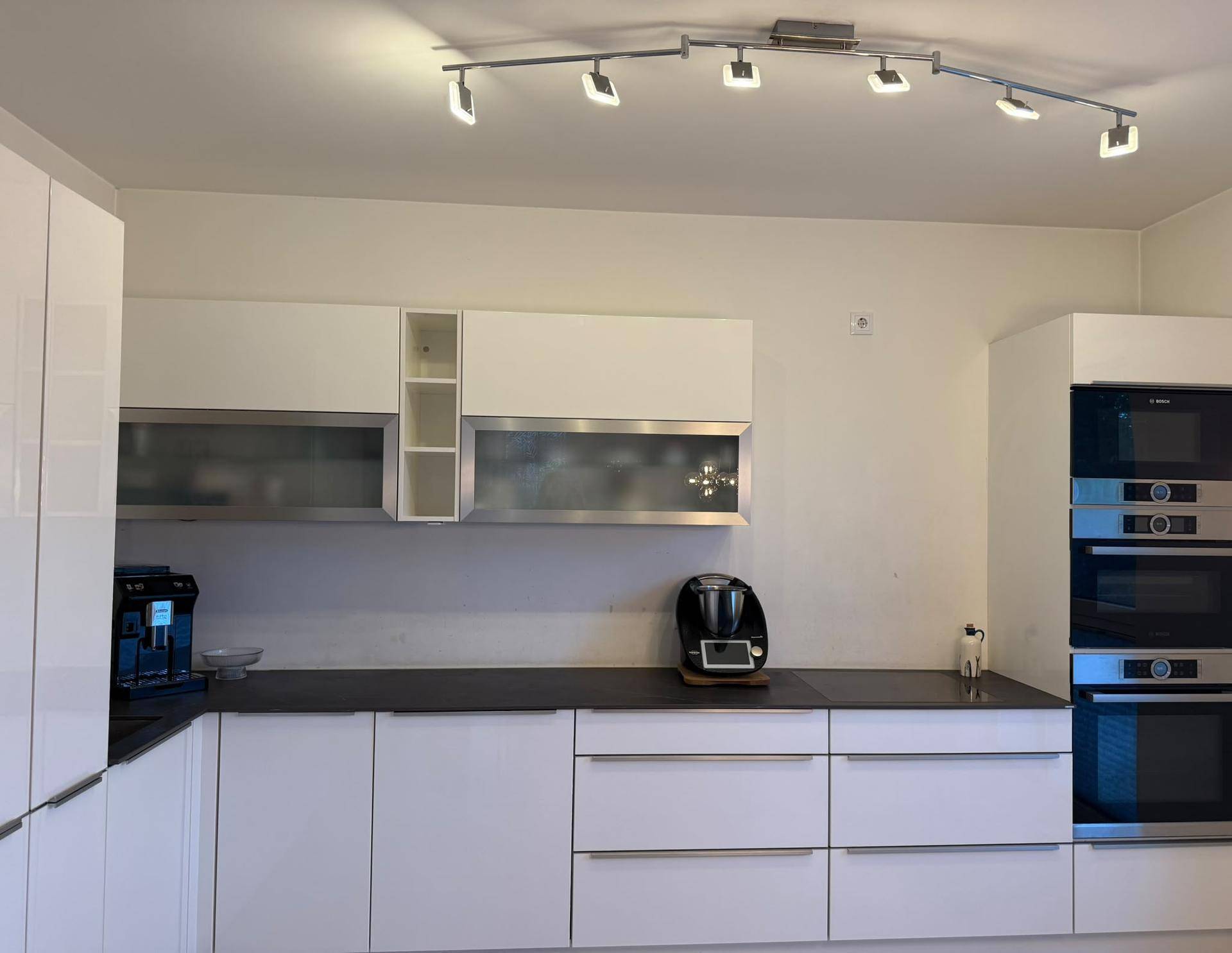 Moderne weiße Küche mit Hochglanzfronten, dunkler Arbeitsplatte und Einbaugeräten.