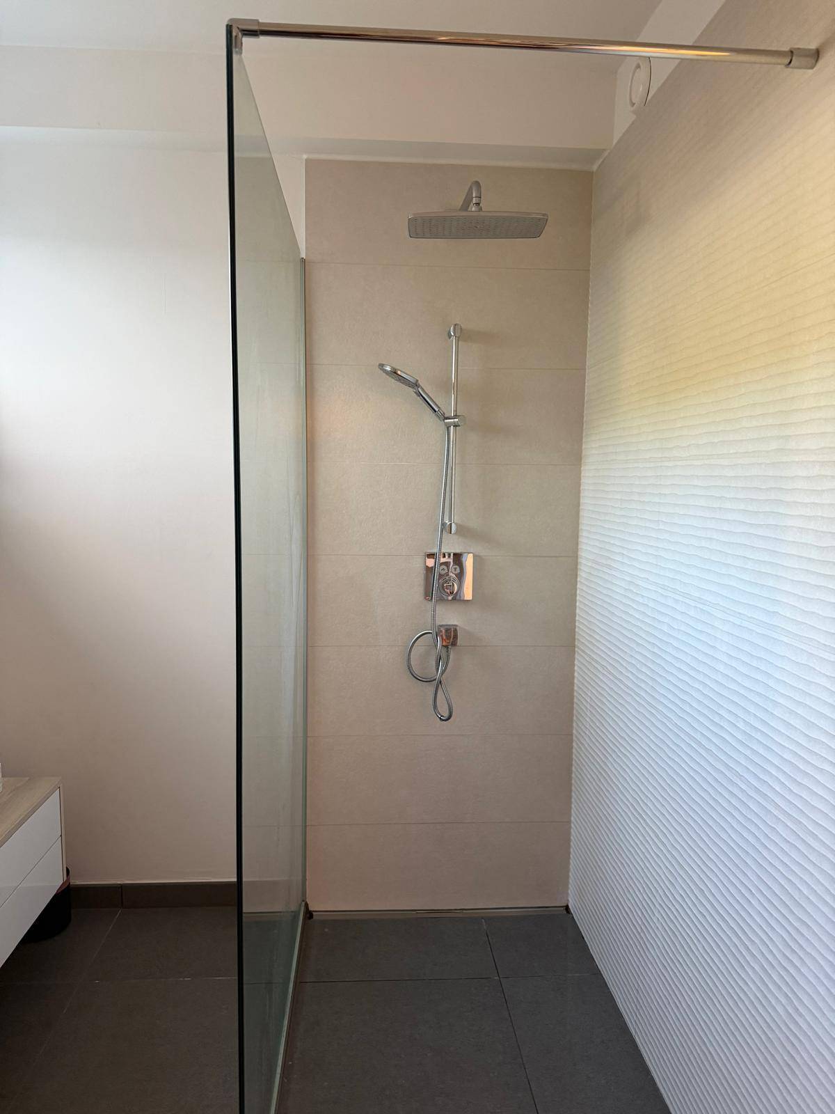 Moderne begehbare Dusche mit Regenduschkopf und hellen Fliesen.