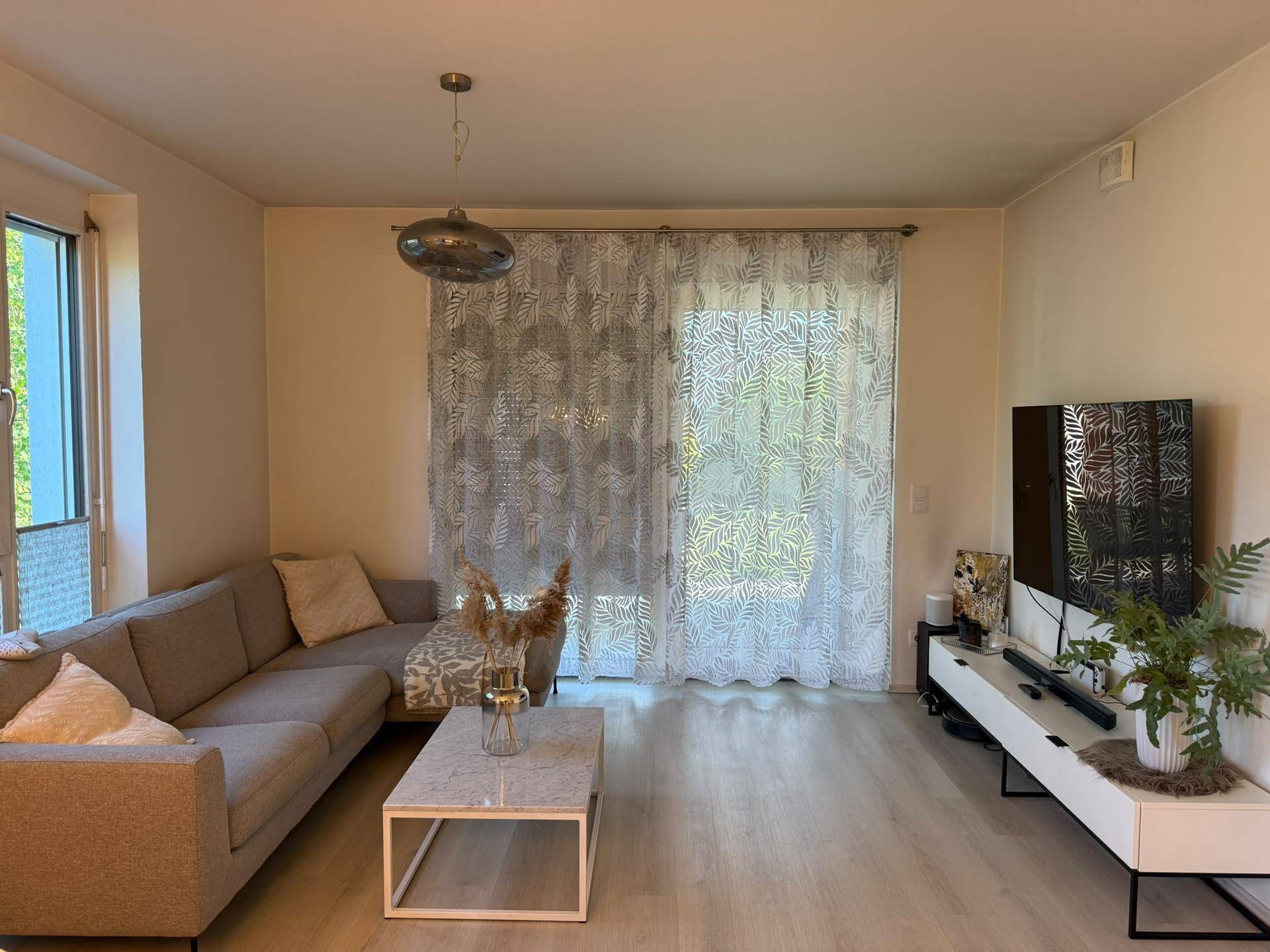 Gemütliches Wohnzimmer mit Ecksofa, Couchtisch und hellem Laminatboden.