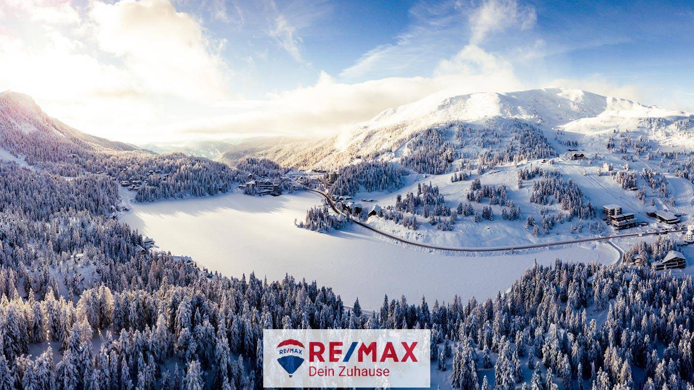Atemberaubende Winterlandschaft aus der Vogelperspektive mit schneebedeckten Bergen und einem zugefrorenen See.