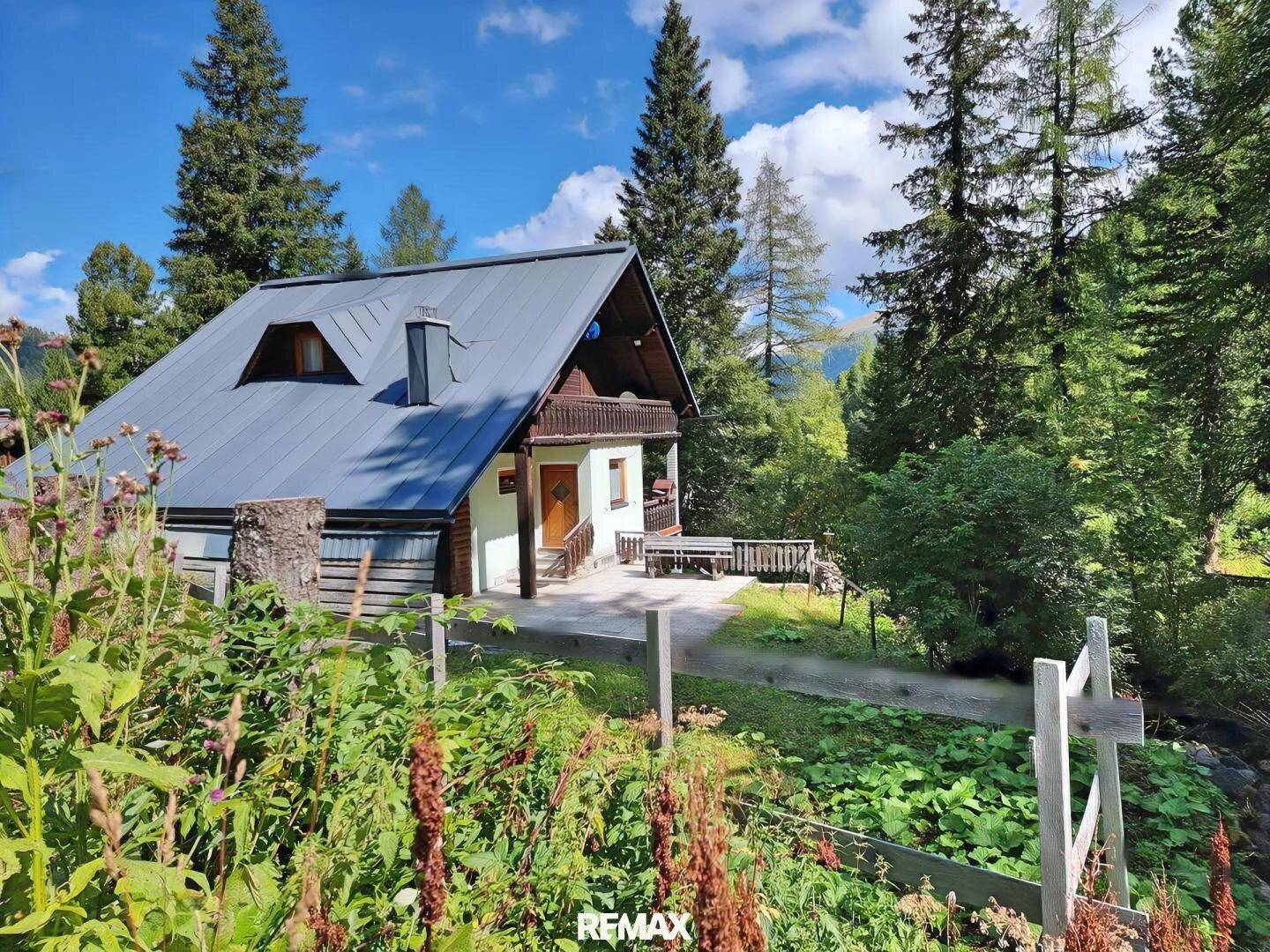 Idyllisches Haus in den Bergen mit Holzbalkon und umgeben von üppiger Natur.