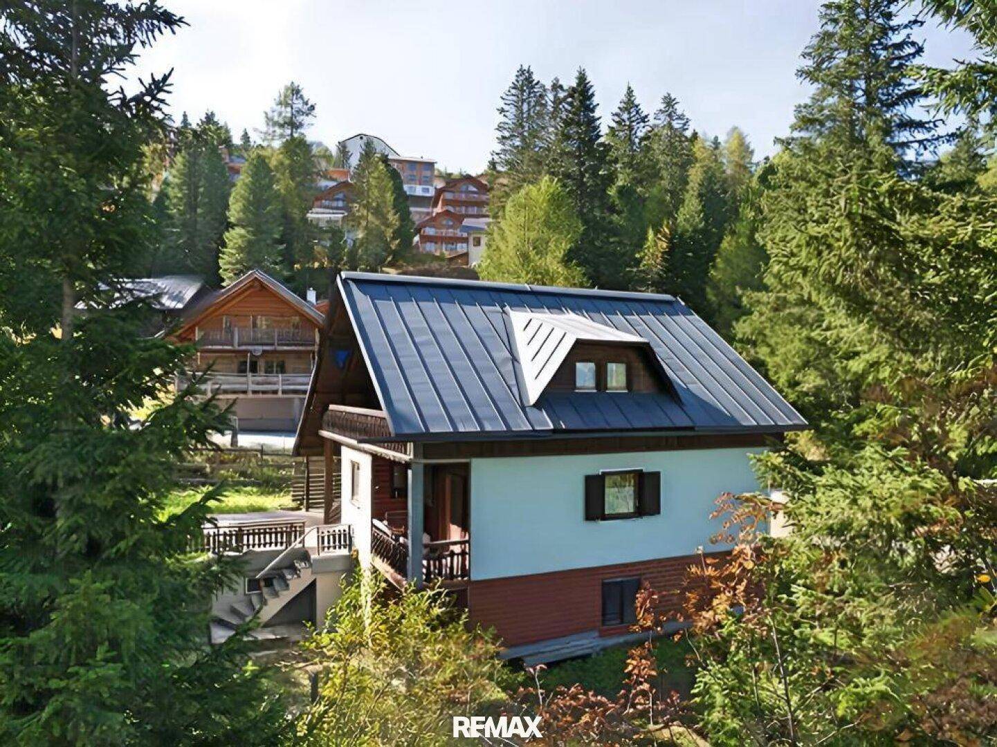 Charmantes Haus im alpinen Stil mit blauem Dach und umgeben von Nadelbäumen.