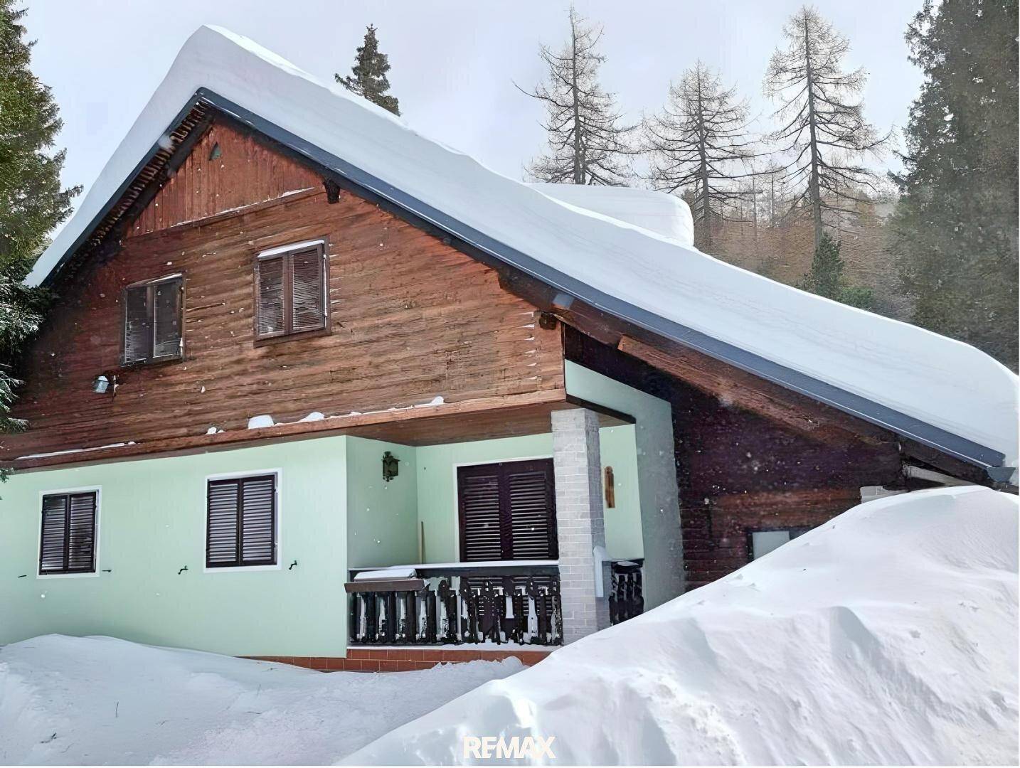 Haus im Winter mit schneebedecktem Dach und umgeben von verschneiten Bäumen.