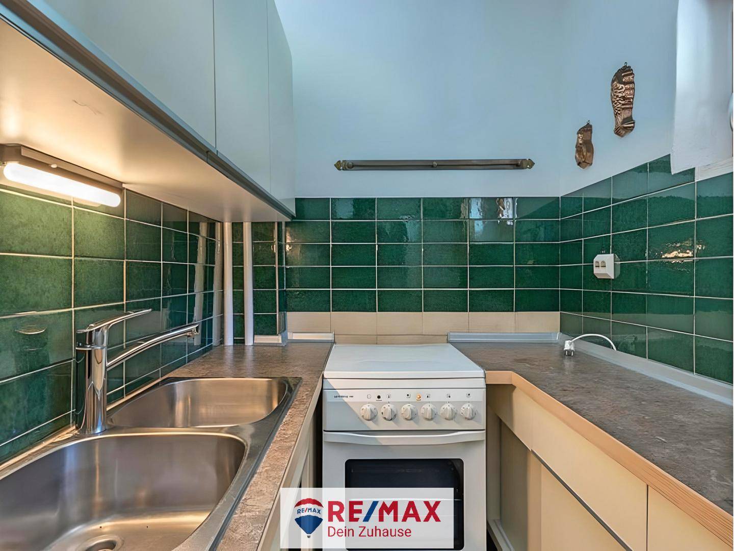 Funktionale Küche mit grünen Wandfliesen, Doppelspüle und einem einfachen Elektroherd.