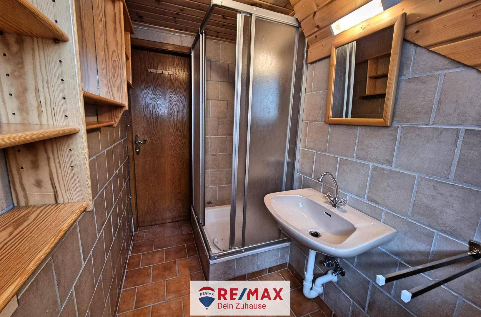 Kleines Badezimmer mit Duschkabine, Waschbecken und braunen Wand- und Bodenfliesen im rustikalen Stil.