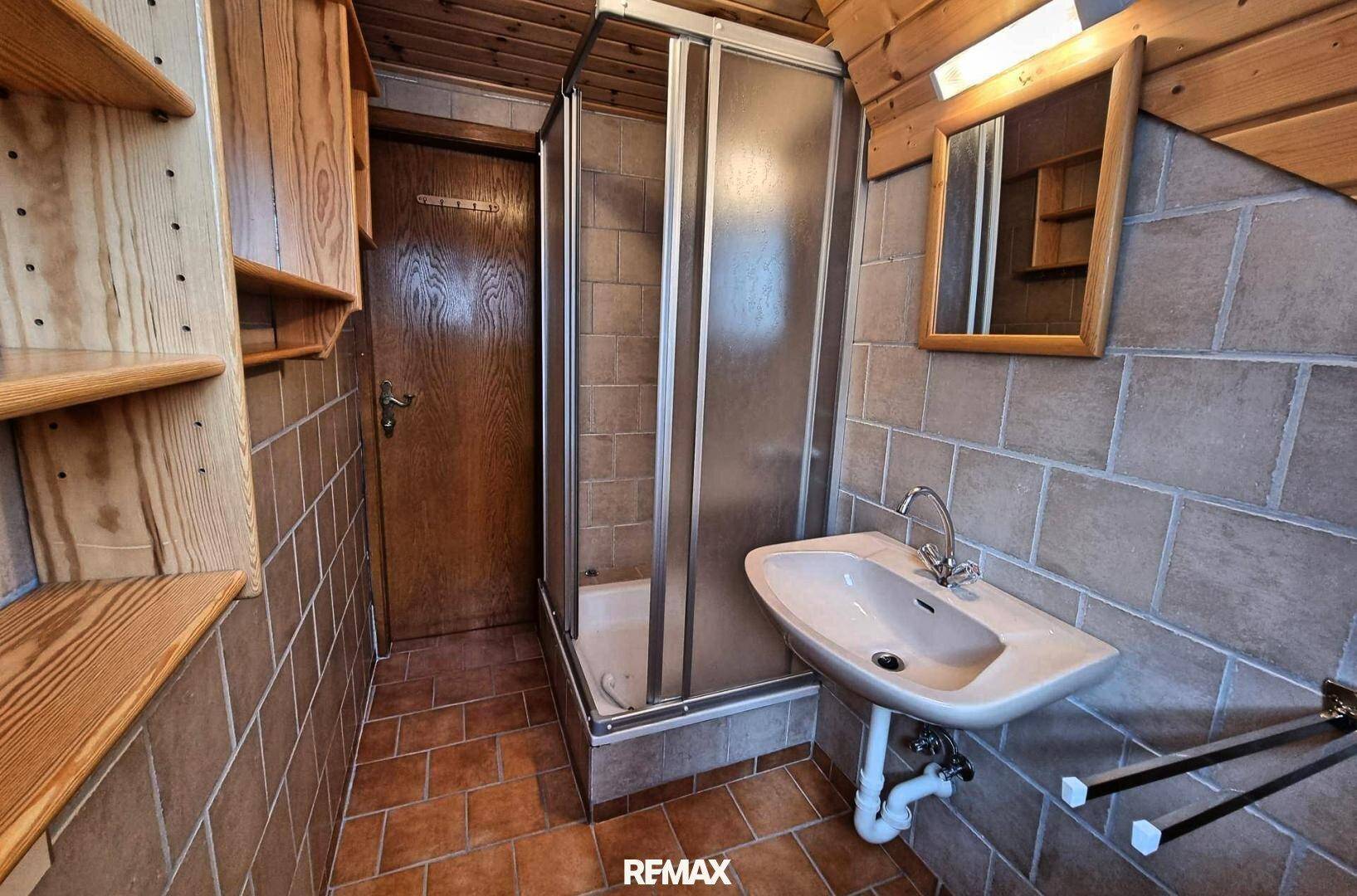 Kleines Badezimmer mit braunen Fliesen, Duschkabine und Holzregalen.