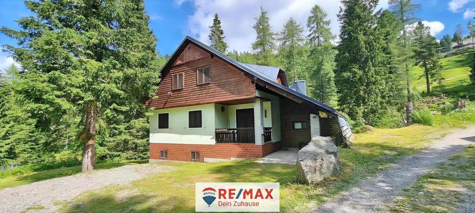 Traditionelles Chalet mit Holzelementen und Satteldach, umgeben von Bäumen und einem Feldweg in der Natur.