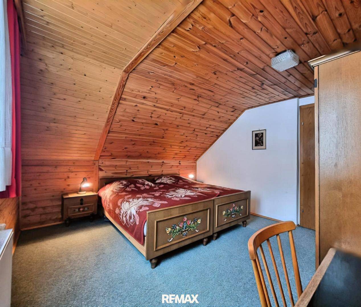 Rustikales Schlafzimmer mit Holztäfelung, Teppichboden und traditionellem Bett.