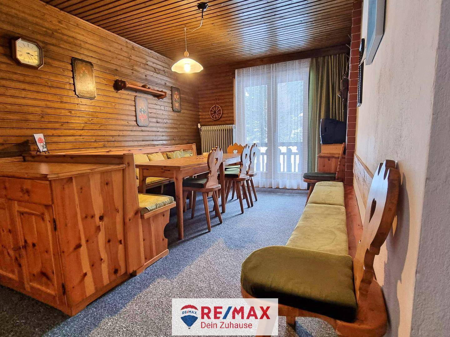 Gemütlicher Essbereich mit Holzwänden, Teppichboden und Fenster mit Blick nach draußen in die Natur.