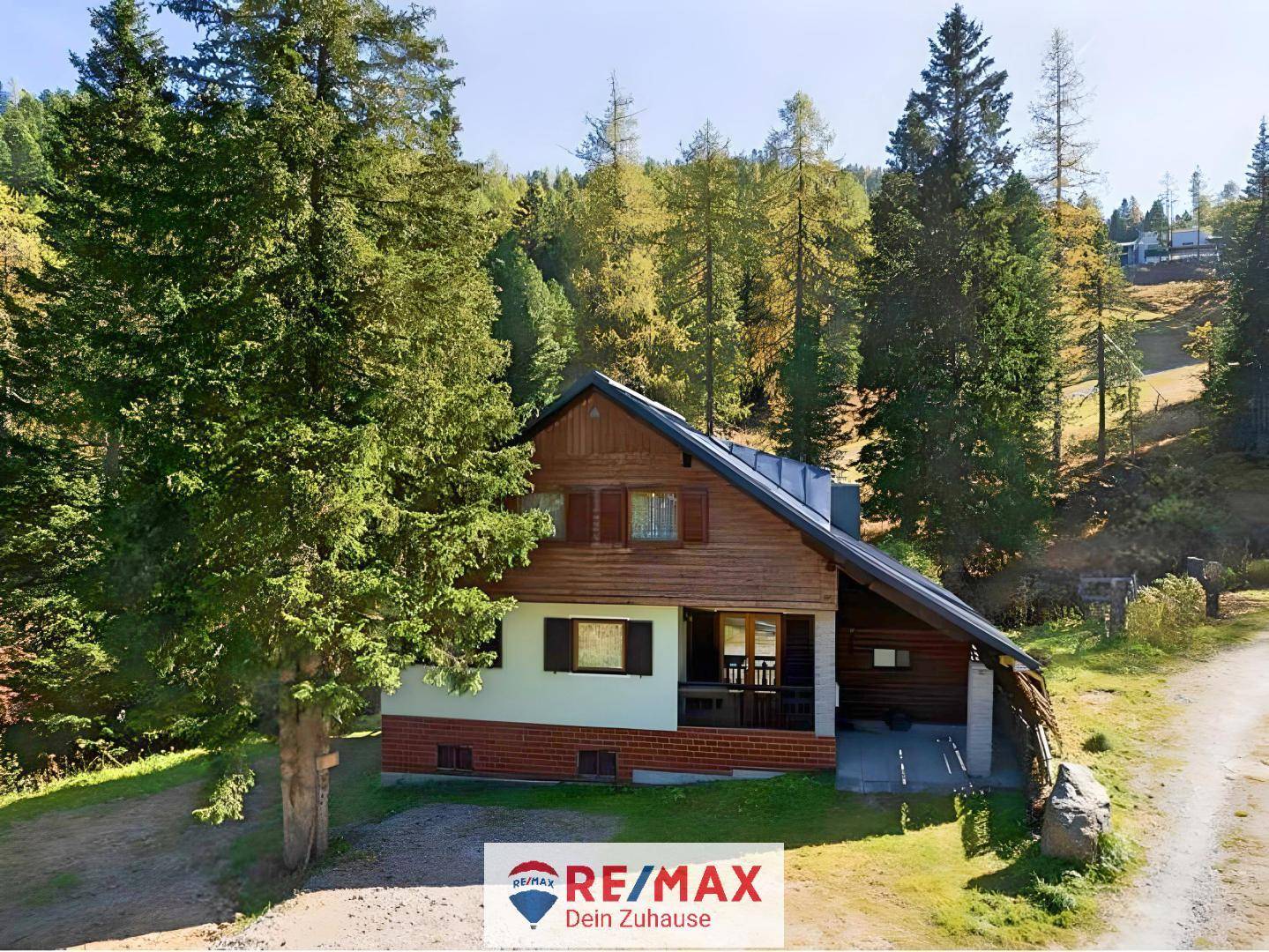 Rustikales Holzchalet in grüner Berglandschaft, umgeben von hohen Bäumen und natürlicher Umgebung.