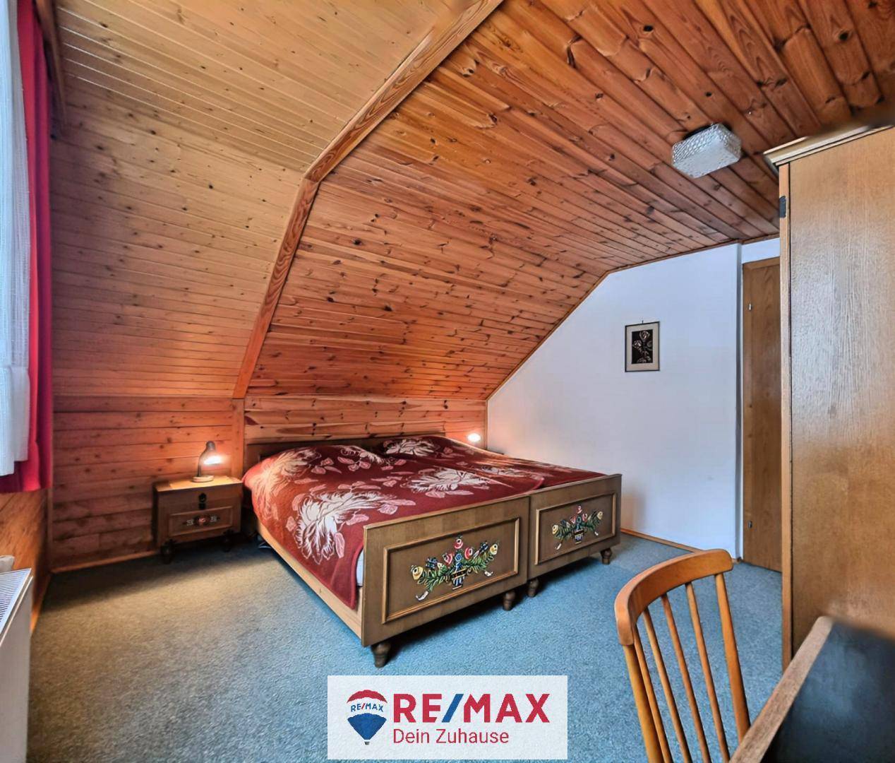 Rustikales Schlafzimmer mit Holztäfelung, Teppichboden und traditionellem Bettgestell unter einer Dachschräge.