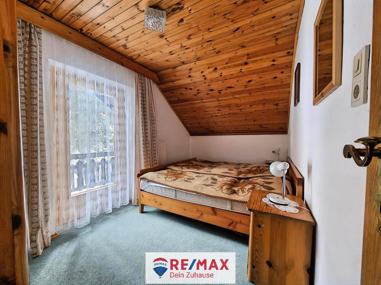 Gemütliches Schlafzimmer mit Holztäfelung, Teppichboden und Zugang zu einem kleinen Balkon mit Bergblick.