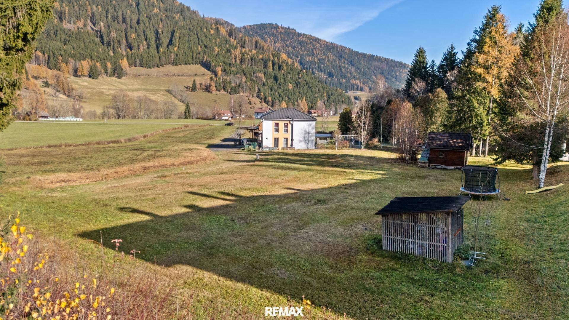 Sonniger Blick über ein weitläufiges Grundstück mit einem Haus, Schuppen und Trampolin im Hintergrund.