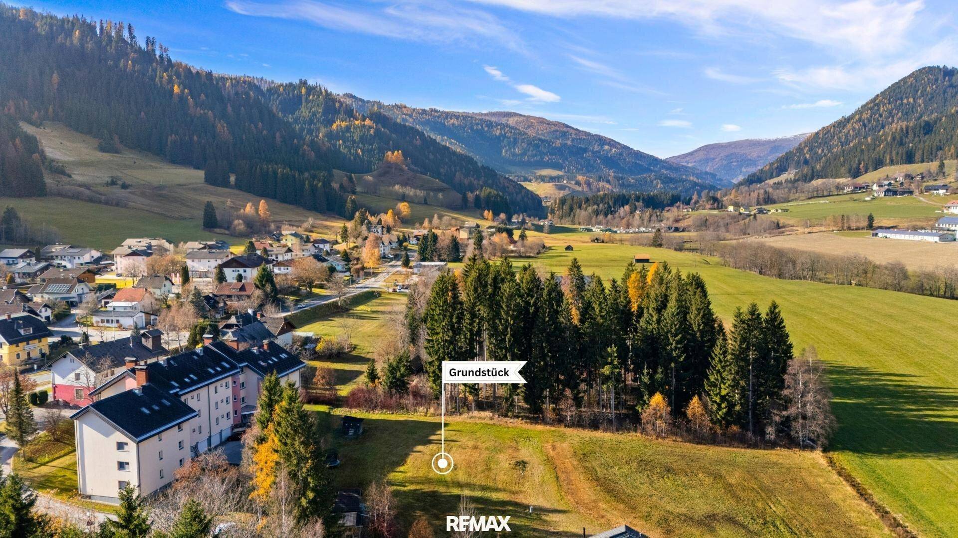 Panoramablick auf ein Dorf in einem Tal mit Bergen im Hintergrund und markiertem Grundstück.