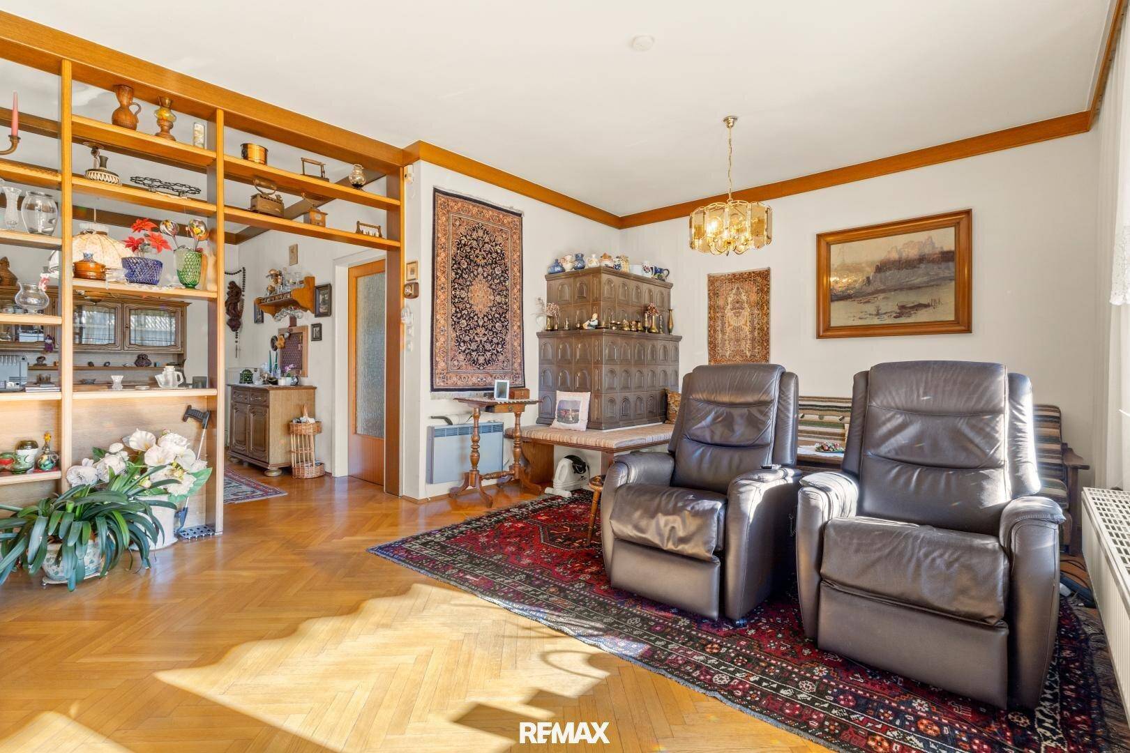 Helles Wohnzimmer mit traditionellem Kachelofen, Holzregalen und bequemen Ledersesseln.