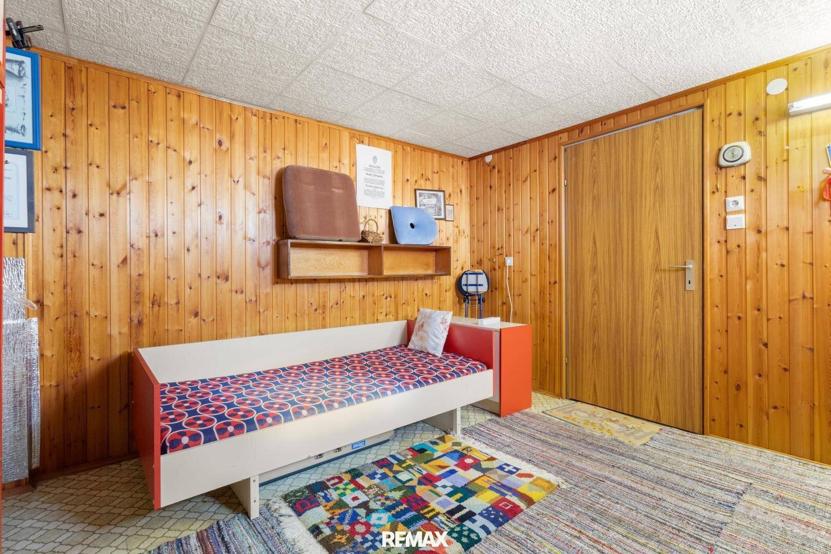Gemütliches Kellerzimmer mit Holzvertäfelung, Einzelbett und farbenfrohem Teppich.