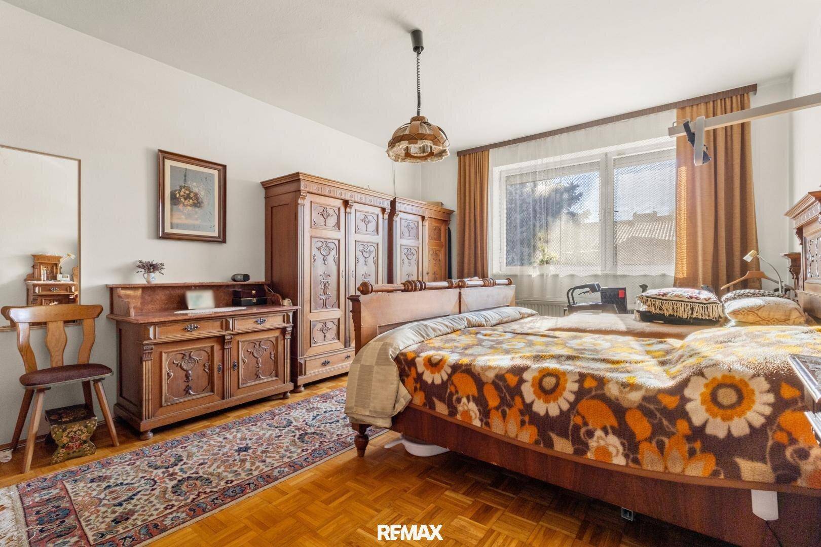 Geräumiges Schlafzimmer mit traditionellen Holzmöbeln, Parkettboden und großem Fenster.