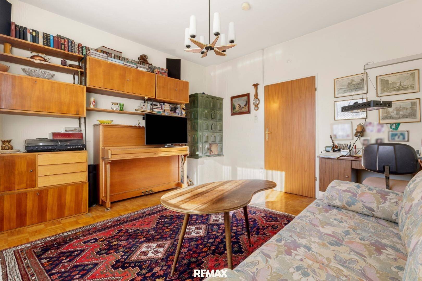 Wohnzimmer mit Sofa, Kachelofen und einer Holzschrankwand mit integriertem Fernseher.