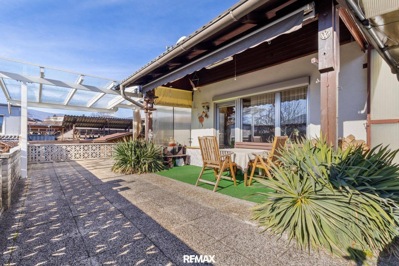 Große, gepflasterte Terrasse mit Sitzgelegenheiten und Pflanzen, teilweise überdacht.