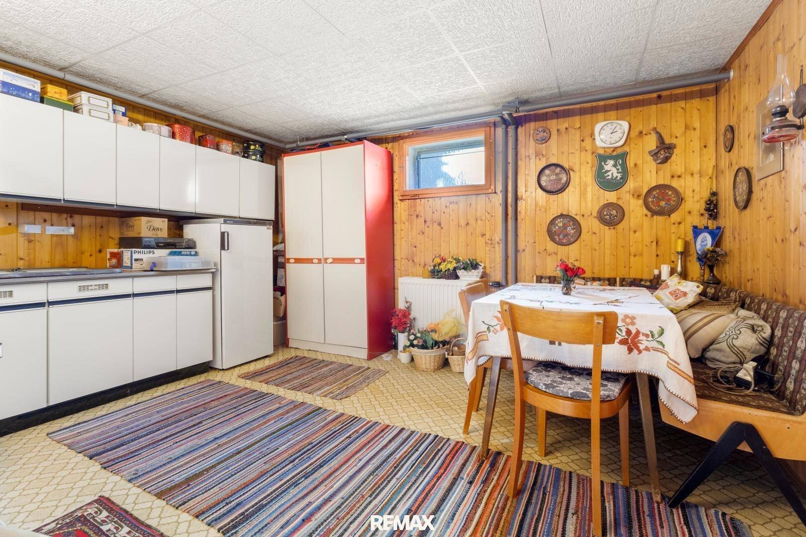 Rustikale Kellerküche mit Holzvertäfelung, einfachen Schränken und einem Essbereich.