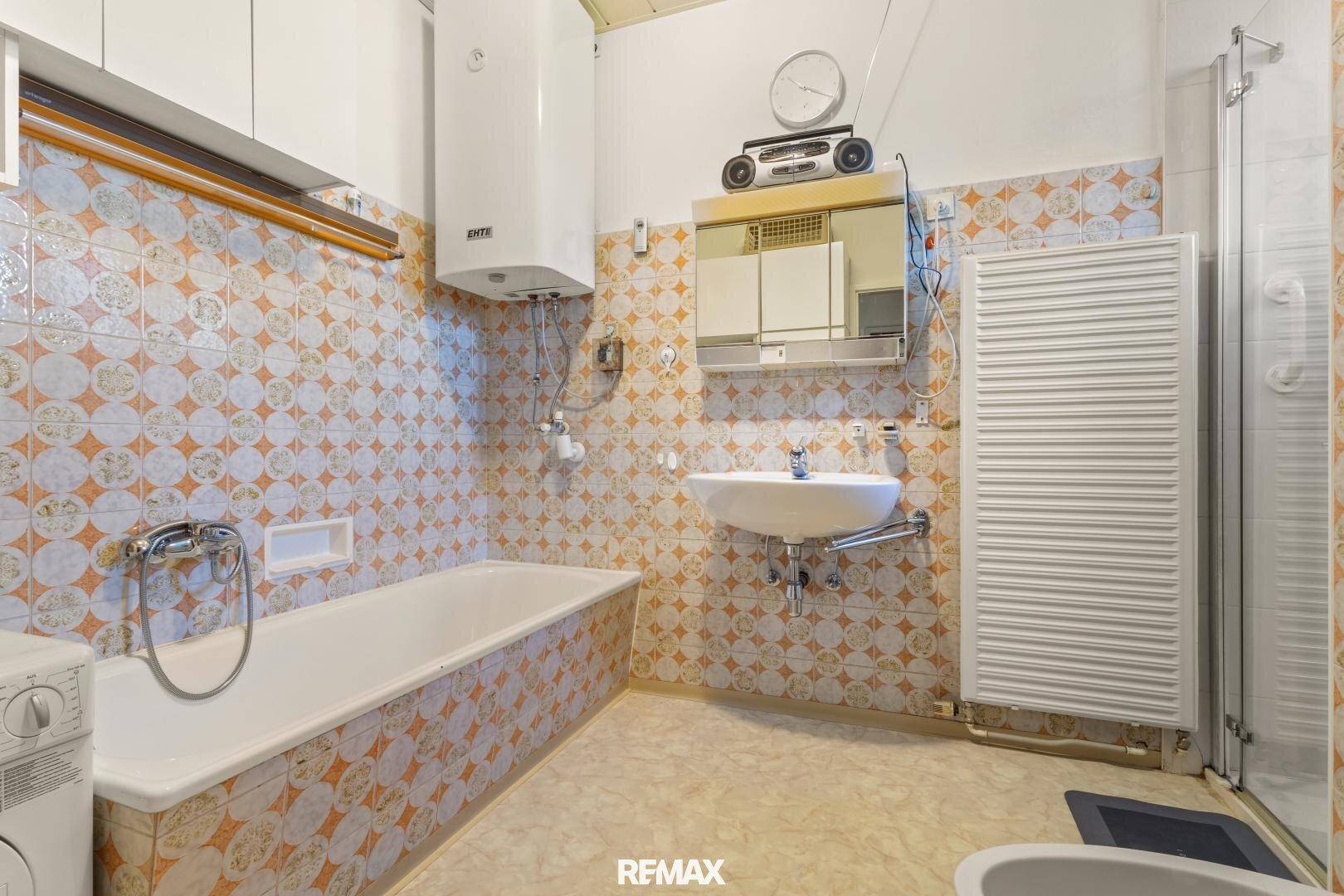 Badezimmer im 80er-Jahre-Stil mit gemusterten Fliesen, Badewanne, Dusche und Einzelwaschbecken.