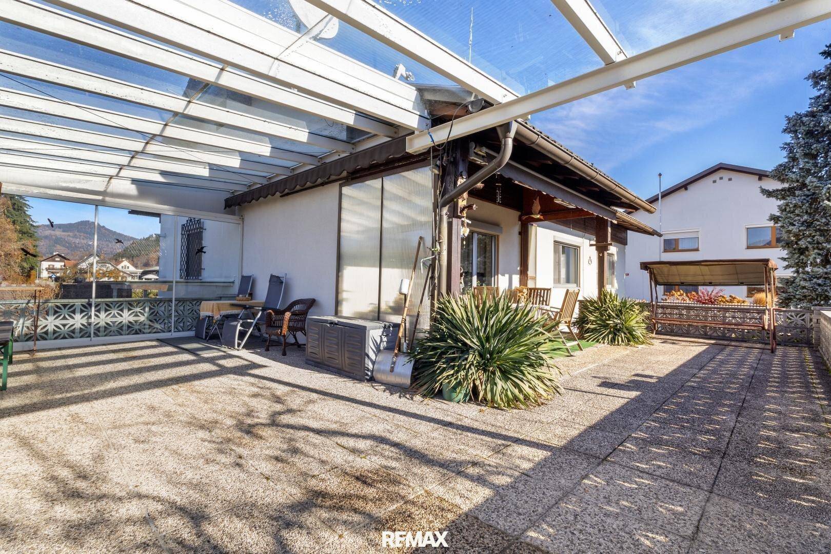 Weitläufige Terrasse mit Glasüberdachung, Schaukel und viel Platz für Entspannung im Freien.