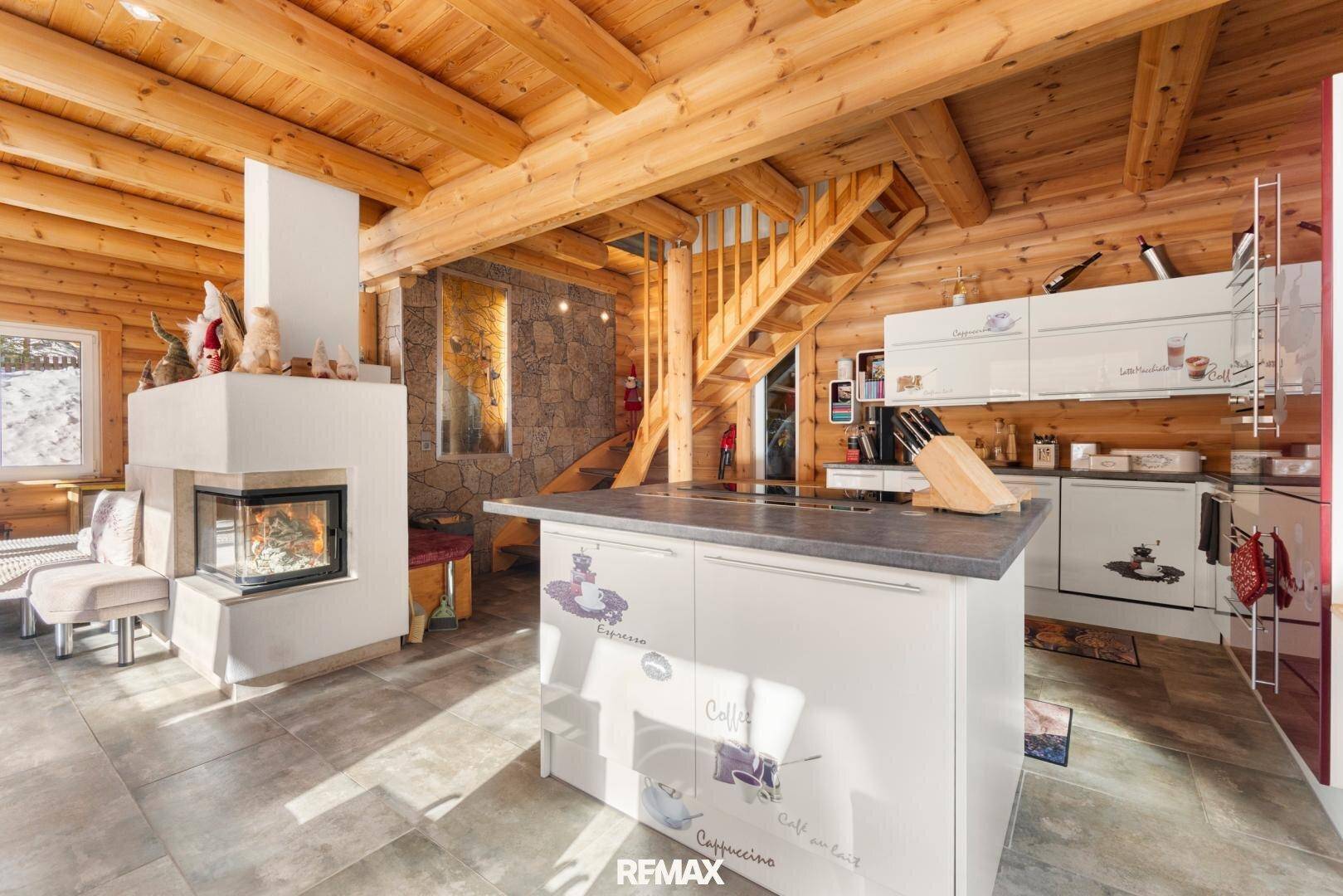 Offener Wohnbereich mit Holzbalkendecke, Kamin, Küche und Treppe in rustikalem Stil.