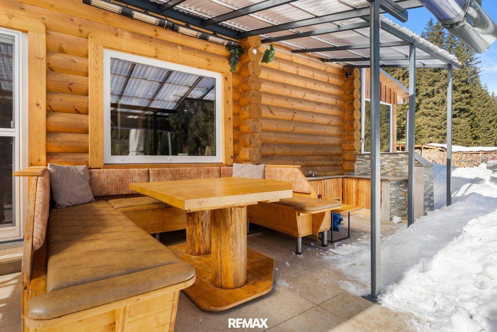 Überdachte Terrasse mit rustikaler Sitzecke und Grillbereich im Schnee.