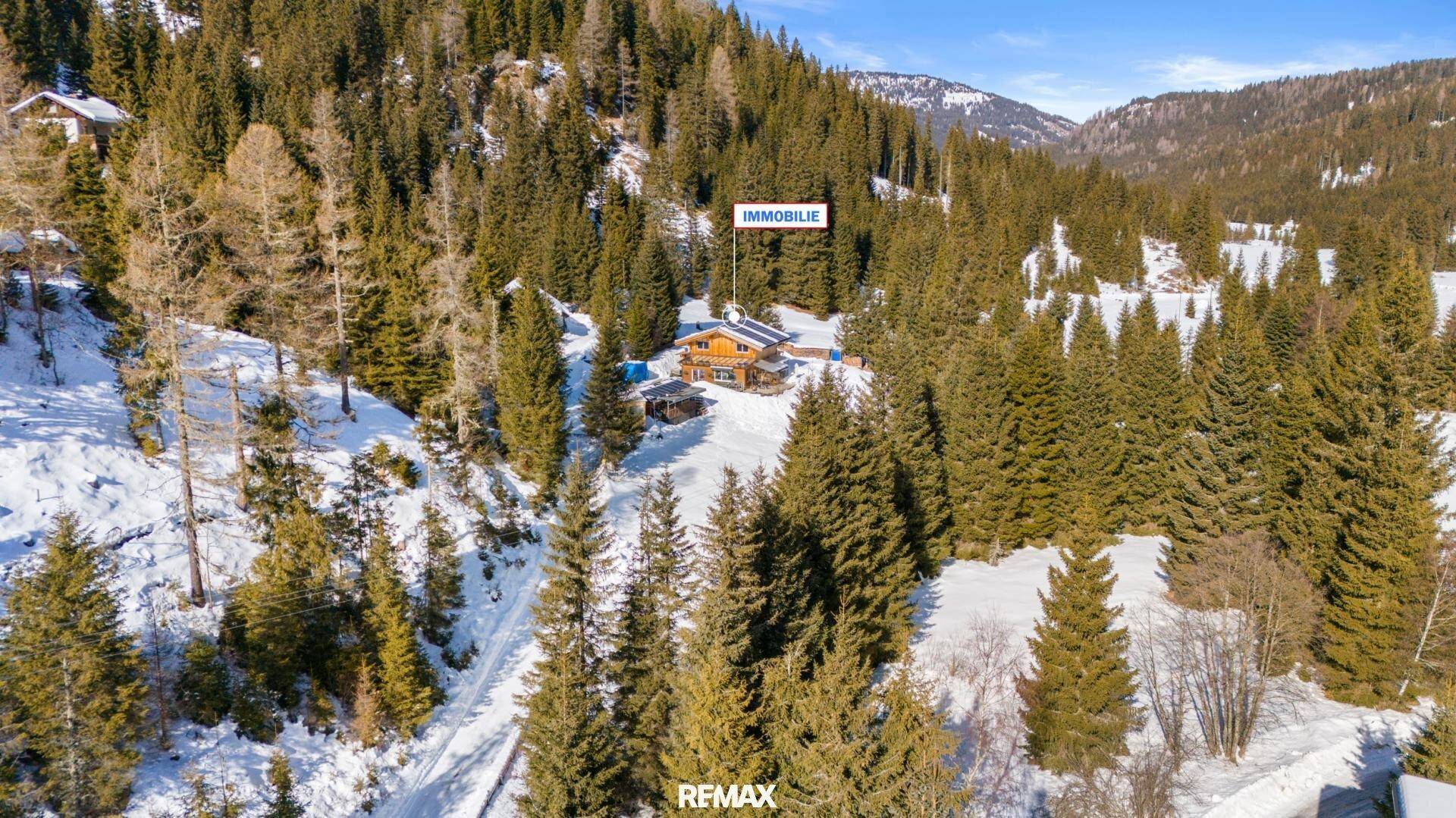 Luftaufnahme des Anwesens in einer verschneiten, bewaldeten Berglandschaft mit klarem Himmel.