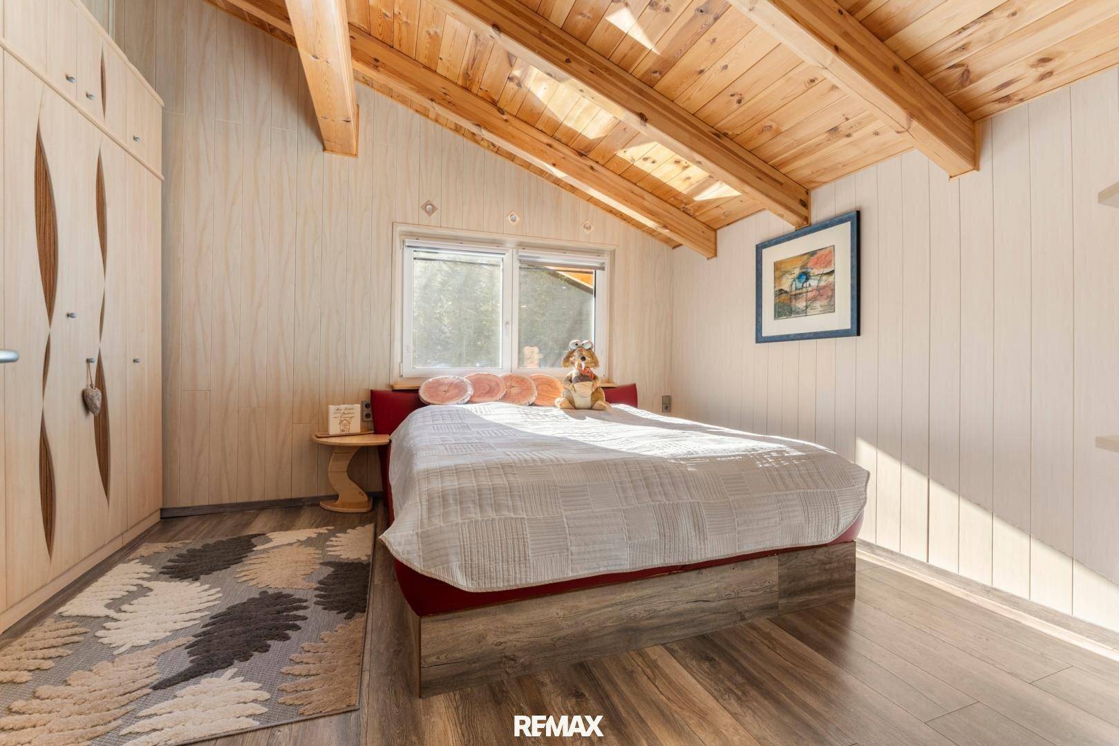 Gemütliches Schlafzimmer mit Holzdachschräge, Holzboden und Fenster mit Bergblick.