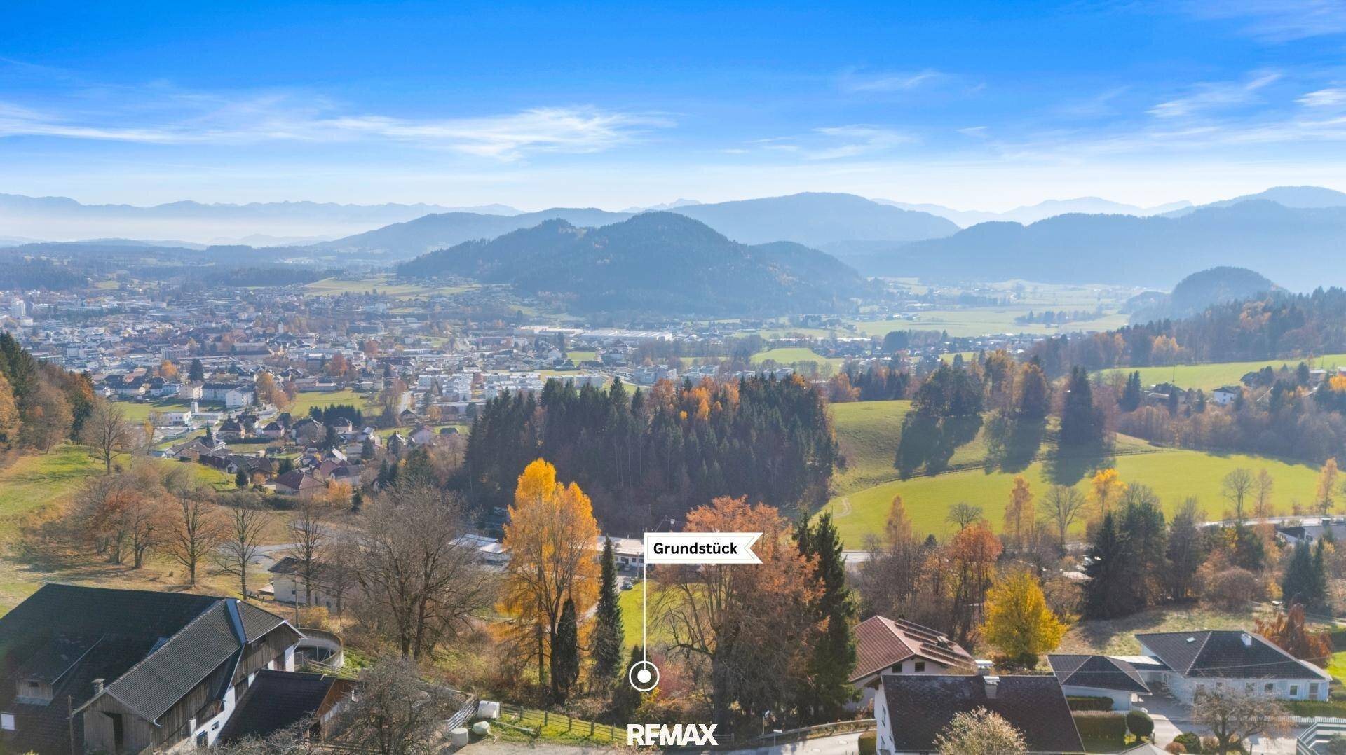 Luftaufnahme eines Grundstücks mit Herbstbäumen, umgeben von ländlicher Bebauung und Bergpanorama.
